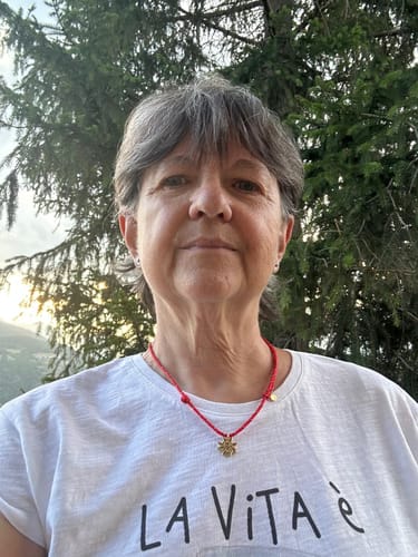 Customer's Collana Stella Alpina di luce with gold pendant on a red cord, worn by a person outdoors near pine trees