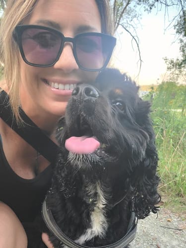 Customer's Dogshood Ergonomic Harness worn by a smiling black dog posing with a person outdoors.