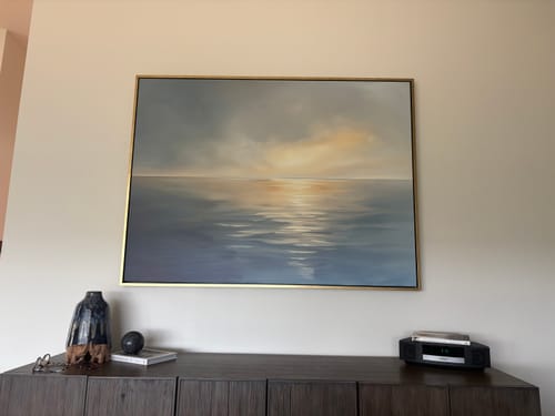 Customer's Luminous Calm canvas art in a gold frame hanging on a wall above a wooden cabinet.