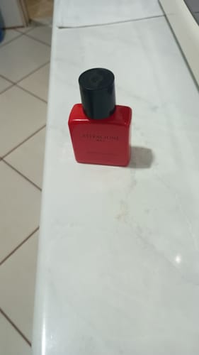 Customer's Attracione Men perfume bottle with a vibrant red finish sitting on a white countertop.