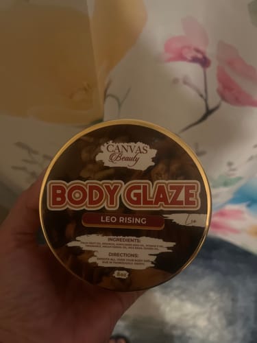 Customer's hand holding a round jar of Canvas Beauty Body Glaze in the Leo Rising scent.
