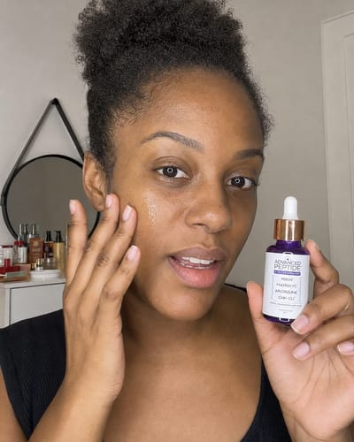 Customer's hand applying Advanced Peptide serum onto cheek, showing glowing, radiant skin texture.