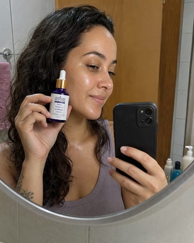 Customer's reflection in a mirror holding the purple Advanced Peptide facial serum bottle.