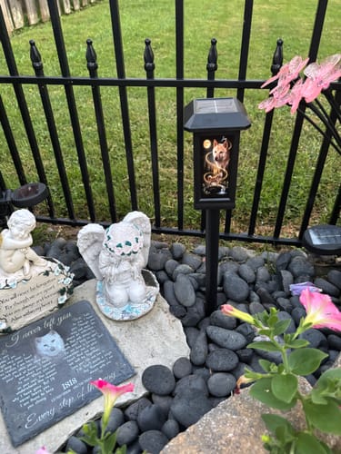 Customer's Dog Howling to the Moon solar light installed in a memorial garden with a statue and stone marker.