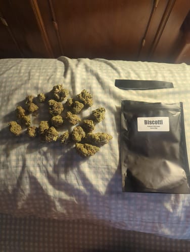 Customer's Biscotti THCA flower buds arranged next to the black product packaging on a white patterned fabric surface.