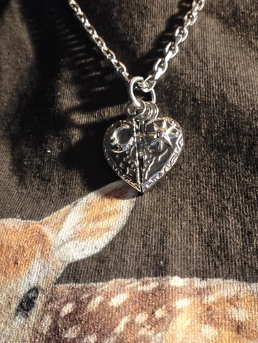 Reviewer's silver Cosmic Heart Pendant hanging from a chain, featuring sun and moon details.