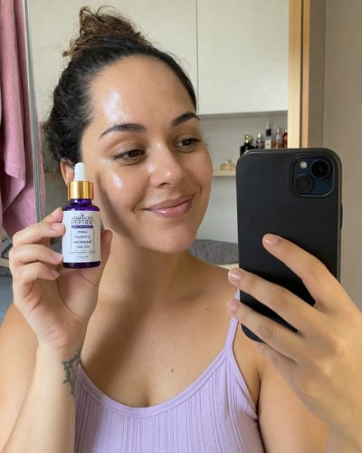 Customer's hand holding the purple Advanced Peptide facial serum bottle with a dropper, showing glowing skin.