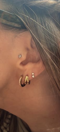 Customer's gold Molten Duo Huggies worn in an ear piercing as part of a stylish stack.