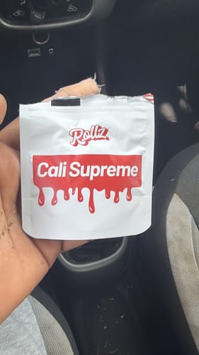 Customer's hand holding the white and red Cali Supreme THC-A flower pouch inside a car.