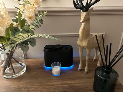 Reviewer's black ZenDuo diffuser with blue LED light on a wooden surface next to flowers and decor.