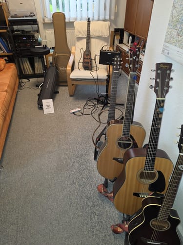 Customer's Donner HUSH X E-Gitarre im Wohnzimmer auf einem Sessel, neben mehreren anderen Akustikgitarren.