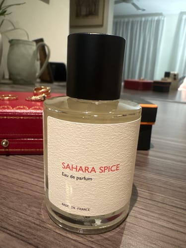 Customer's Sahara Spice fragrance bottle with a black cap, standing on a wooden surface.