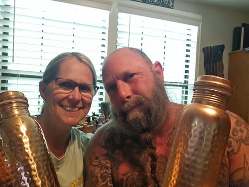 Customer's hand-hammered copper water bottles held by two smiling people