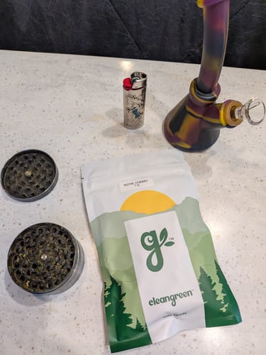Customer's Royal Cherry product packaging next to a silicone bong, lighter, and grinder on a light counter.