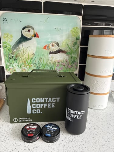 Customer's black Timemore Travel Coffee Maker next to a branded green metal box and two coffee tins on a kitchen counter.
