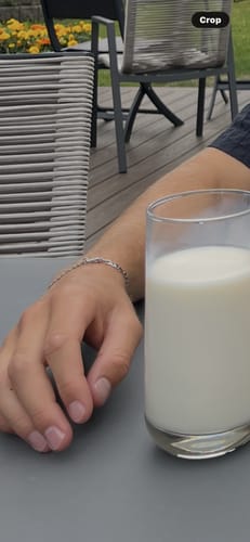 Customer's silver Figaro link ID bracelet worn on a person's wrist, sitting at an outdoor table with a glass of milk.