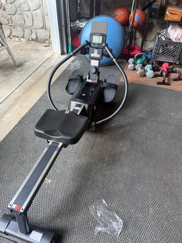 Customer's rowing machine with independent oars and digital display, set up on a gym mat in a garage.