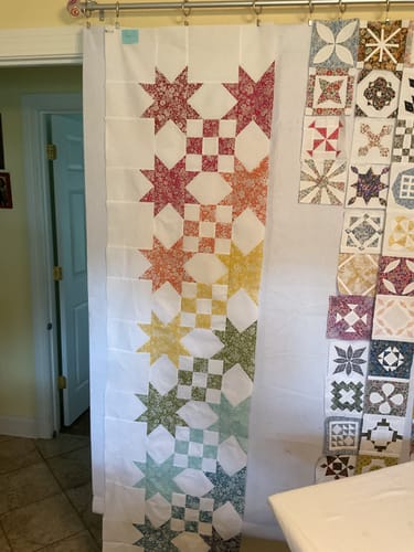 Customer's Star Studded Quilt Kit pieces pinned in a colorful pattern against a white wall.