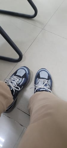 Customer's feet wearing blue and grey Retrograde sneakers with white laces, seen from a high angle while sitting.