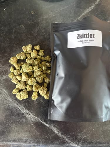 Customer's Zkittlez THCA flower in a sealed black bag next to a small pile of light green cannabis buds on a counter.