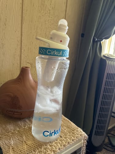 Reviewer's clear plastic Cirkul water bottle with blue comfort grip lid sitting on a textured table.
