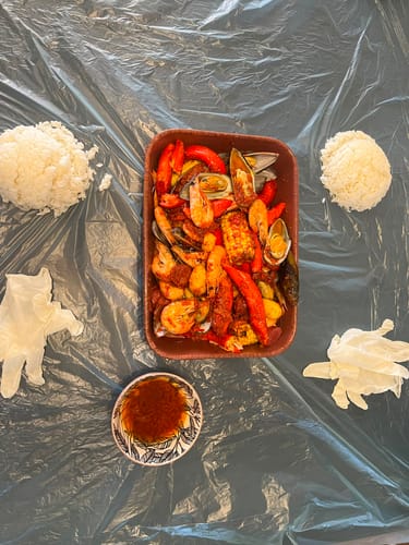 Reviewer's Cajun Seafood Boil Bomb meal with shrimp, corn, and shellfish served on a plastic sheet with rice and gloves.