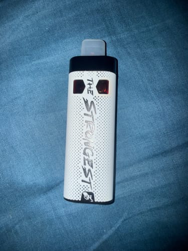 Customer's white THE STRONGEST disposable vape pen on a textured blue surface.