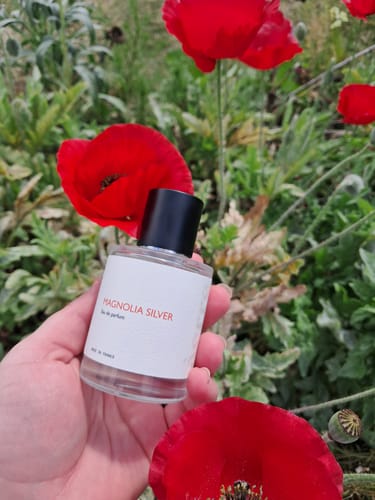 Customer's hand holding a bottle of Magnolia Silver perfume against a background of bright red poppies.