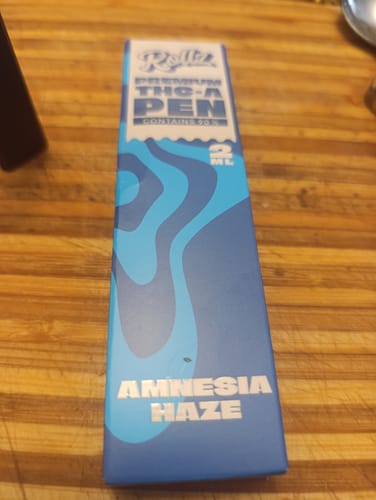 Customer's blue and white THC-A Vape packaging labeled Amnesia Haze on a wooden surface.
