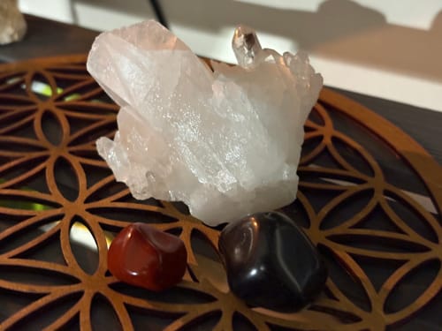 Customer's Pierre Onyx stone next to a red jasper stone and a white quartz cluster on a wooden flower of life grid.