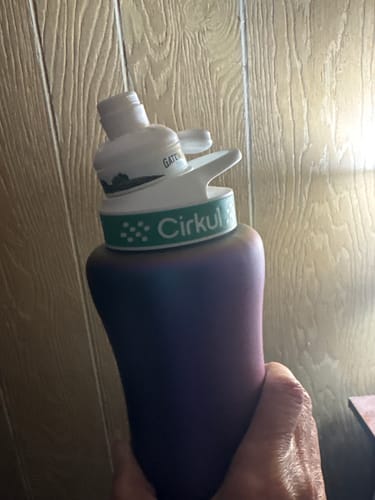 Customer's hand holding a Gateway Blackberry Tea Cirkul bottle with a white cap against a wood-paneled wall.