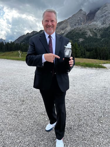 Customer's GoSip Black Cherry bottle held by person in a suit, pointing at it with a mountain landscape background