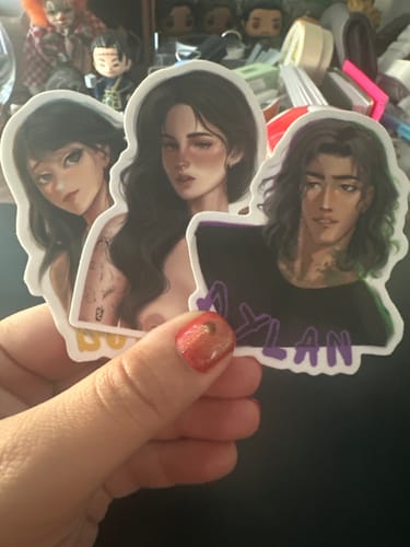 Customer's hand holding three high-quality, custom vinyl stickers featuring illustrated characters.