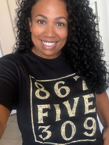 Reviewer smiling while wearing the black ADHD Rock T-Shirt with the iconic 867-5309 design in gold text.