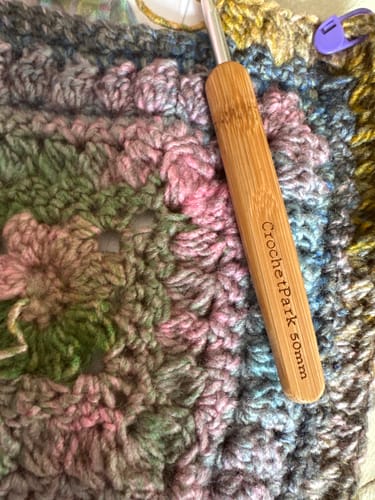 Customer's Crochetpark bamboo crochet hook resting on colorful, crocheted yarn fabric.