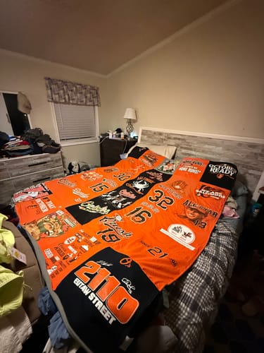 Customer's Project Repat T-Shirt Quilt displayed on a bed, showing orange and black athletic jerseys.