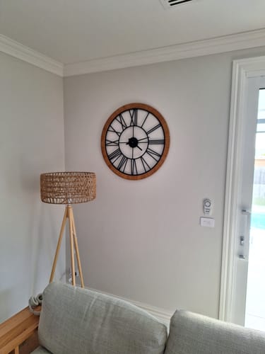 Customer's Hugo French Country Wall Clock with rattan frame and black iron numerals mounted on a light wall