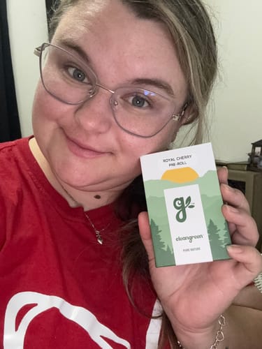 Reviewer holding a Royal Cherry Pre-Roll box featuring a nature-themed design with mountains and trees.