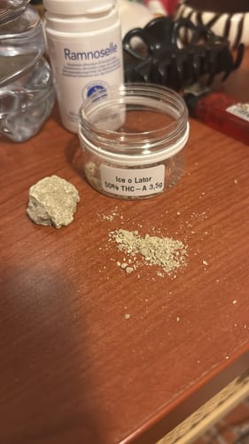 Customer's THC-A 50% Hash Ice o Lator pieces and a small pile of powder on a brown surface next to an open jar.