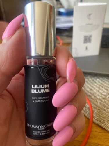 Customer's hand with pink nails holding a glass Lilium Blume perfume bottle.