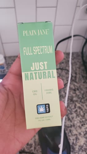 Reviewer holding a box of Plain Jane Full Spectrum CBD oil tincture, 1000mg, in a light green package.