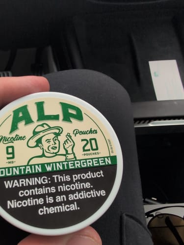 Customer's hand holding a round tin of ALP Mountain Wintergreen nicotine pouches, showing the branding and warning label.