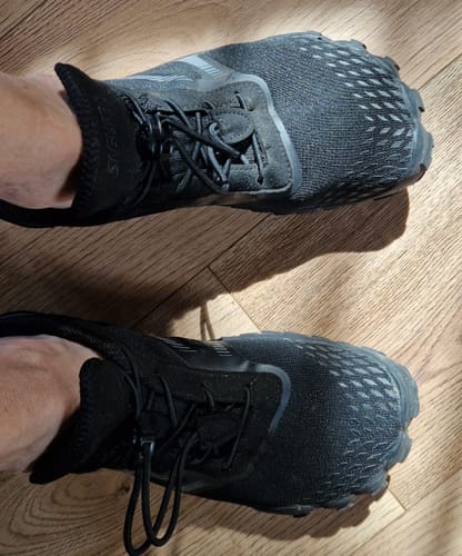 Customer's feet wearing black Motion I Pro barefoot shoes on a wooden floor.
