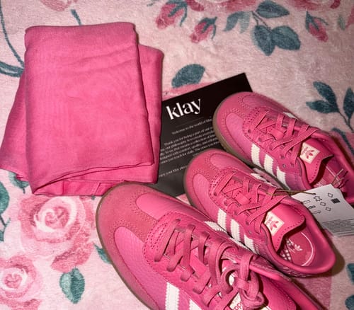 Reviewer's Pink Peony Premium Modal hijab folded next to matching vibrant pink sneakers on a rose-patterned surface.