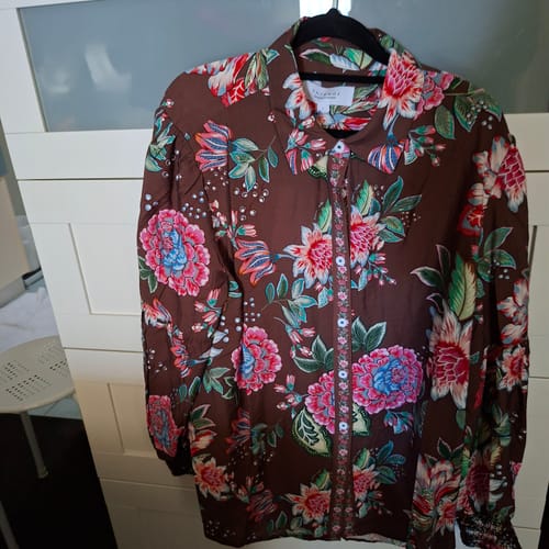 Customer's Bouquet Floral Print Shirt hanging on a hanger, showing vibrant flowers on brown fabric.