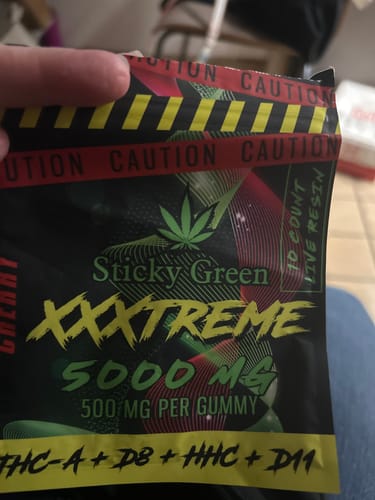 Customer's hand holding a black XXXtreme Gummies pouch with bold red caution tape branding.