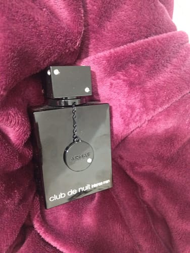 Customer's black Armaf Club de Nuit Intense Man perfume bottle resting on a soft, dark red fabric surface.