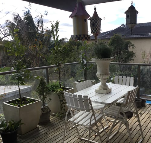 Customer's antique white Florentine Medici Urn Planter standing on a wooden outdoor dining table.