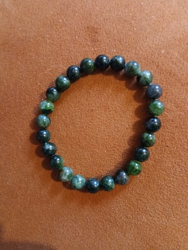 Customer's bracelet de diopside chromifère, montrant des perles de différentes nuances de vert sur une surface brune.