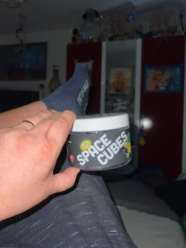 Customer's hand holding a jar of THC Space Cubes, label clearly visible, in a relaxed home setting.